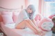 A woman sitting on a bed with a pink teddy bear.