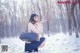 A woman kneeling in the snow blowing a snow ball.